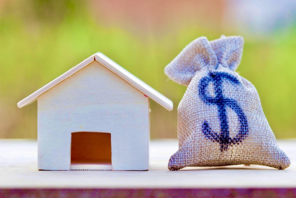 US dollar in a money bag, small residential, house model on table against green nature background.